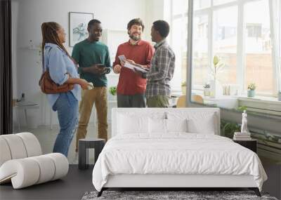 Full length portrait of multi-ethnic group of people dressed in casual wear and smiling cheerfully while discussing work standing in office Wall mural