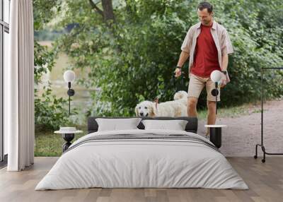 Full length portrait of smiling man walking dog outdoors in Summer at green park, copy space Wall mural