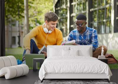 Full length portrait of two college students studying outdoors sitting on green grass in campus, copy space Wall mural