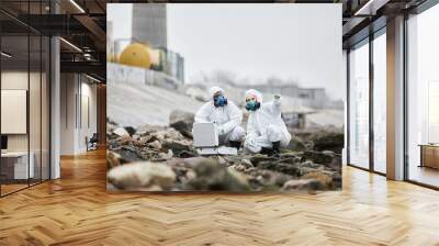 Full length portrait of two workers wearing hazmat suits collecting probe samples in industrial area, toxic waste concept Wall mural