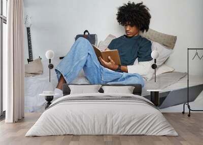 Full length portrait of young African-American man sitting on bed at home and writing in notebook, copy space Wall mural