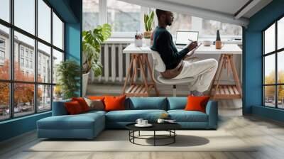 Full length side view portrait of young African-American man wearing glasses while working from home, copy space Wall mural