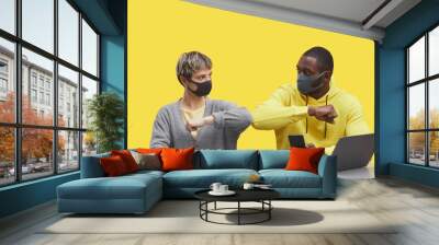 Graphic portrait of two modern business people wearing masks and bumping elbows while working together at desk against pop yellow background, copy space Wall mural