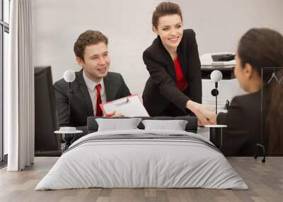 Group of business people discussing partnership at meeting in modern office, focus on smiling businesswoman shaking hands with new client while man showing contract to her Wall mural