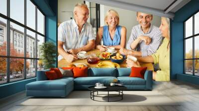 Group of mature people chatting cheerfully while sitting around table in kitchen, copy space Wall mural