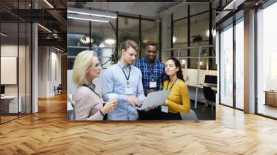 Group of multi-ethnic business colleagues standing in modern office and using portable computer while discussing internet project Wall mural