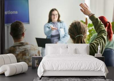 Group of participants engaging in interactive business seminar, with one individual raising hand while seated and another person presenting in background with laptop Wall mural