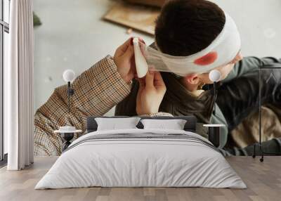 High angle of nurse bandaging head of wounded civilian man in refugee shelter, copy space Wall mural