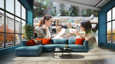 High angle portrait of two modern young women sitting at table in designer cafe and smiling cheerfully while discussing business, copy space Wall mural