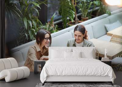 High angle portrait of two young women working together sitting at table in outdoor cafe terrace decorated with plats, copy space Wall mural