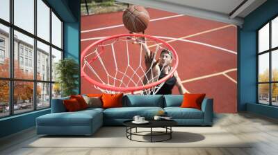 High angle  portrait of young basketball player throwing ball in hoop and scoring on outdoor court lit by sunlight, copy space Wall mural