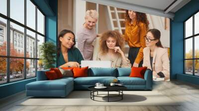 Horizontal portrait of five charming female colleagues watching something on laptop while working on business project together Wall mural