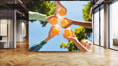 Low angle close up of kids holding glasses with orange juice against blue sky outdoors, copy space Wall mural