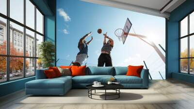 Low angle  of two young men playing basketball and jumping by hoop against blue sky, copy space Wall mural