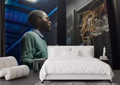 Low angle portrait of African American data engineer holding digital tablet while working with supercomputer in server room lit by blue light, copy space Wall mural