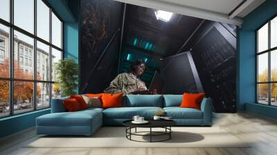 Low angle portrait of young African-American woman wearing military uniform using laptop while standing in server room, copy space Wall mural