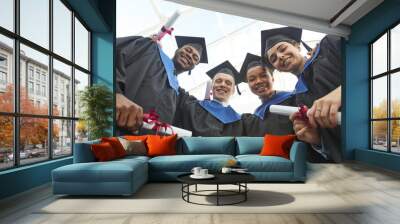 Low angle view at diverse group of happy young people wearing graduation gowns and holding diplomas while looking down at camera Wall mural