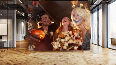 Low angle view at group of friends enjoying Halloween party in nightclub, focus on smiling young woman having fun Wall mural