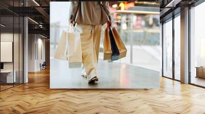 Low section of unrecognizable woman wearing pants and holding blank shopping bags while walking in mall, copy space Wall mural