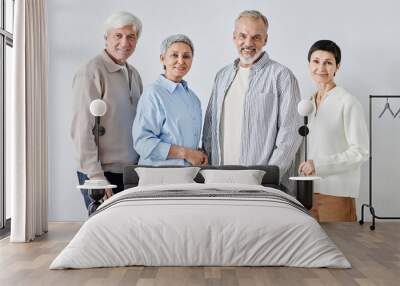 Medium long shot of two female and two male senior people in casual clothes smiling and looking at camera while standing against white background Wall mural