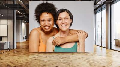 Minimal waist up portrait of two real women embracing and smiling happily against grey background Wall mural