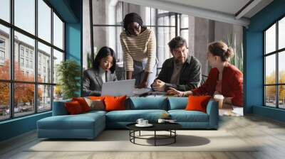 Multi-ethnic group of business people discussing project while sitting at meeting table in graphic office interior Wall mural