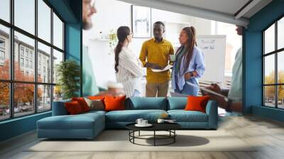 Multi-ethnic group of creative business people chatting during break in conference room, focus on smiling African-American man talking to women dressed in casual wear, copy space Wall mural