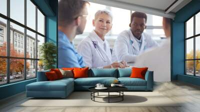 Multi ethnic group of doctors sitting at table, focus on mature woman heading committee meeting at medical council Wall mural