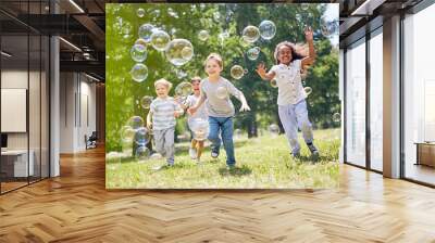 Multi-ethnic group of little friends with toothy smiles on their faces enjoying warm sunny day while participating in soap bubbles show Wall mural