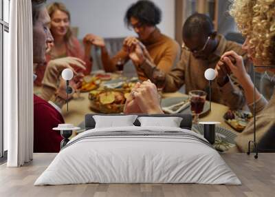 Multi-ethnic group of people holding hands while praying at Thanksgiving dinner with friends and family, focus on foreground, copy space Wall mural