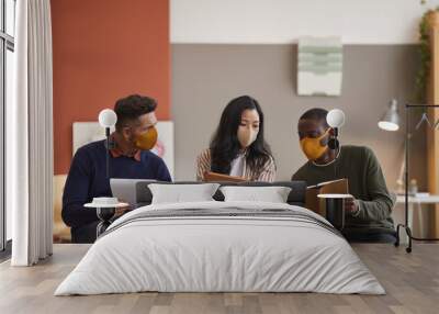 Multi-ethnic group of three business people wearing face masks while discussing project in office Wall mural