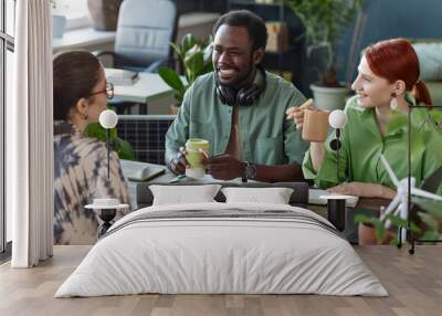 Multiethnic team of smiling young business people collaborating in office sitting at meeting table in green office Wall mural