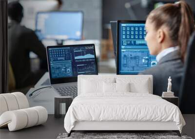 Over shoulder view of female IT security specialist using multiple computers with blue data on screen copy space Wall mural