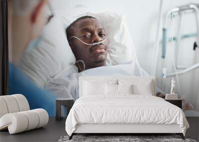 Portrait of African-American man lying in hospital bed and looking at doctor, copy space Wall mural