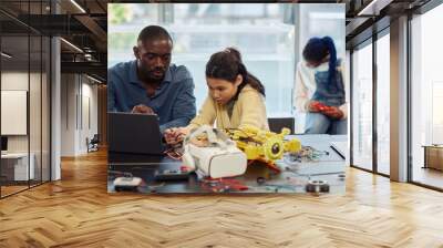 Portrait of Asian teenage girl building robots in engineering class and using laptop with male teacher helping, copy space Wall mural