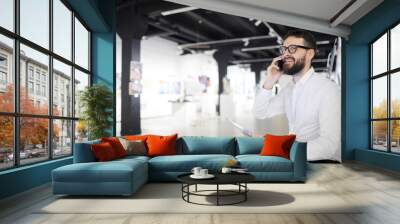 Portrait of bearded art gallery manager speaking by phone while preparing for exhibition in museum, copy space Wall mural