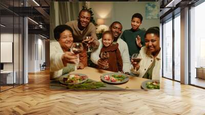 Portrait of big African-American family raising glasses at camera while enjoying Christmas dinner together Wall mural