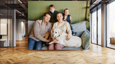 Portrait of big happy family with two kids and dog sitting on couch at home against green wall, copy space Wall mural