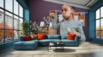 Portrait of Black little girl blowing soap bubbles indoors and having fun, copy space Wall mural