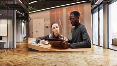 Portrait of black young businessman talking to female colleague while discussing workin hall at modern office building Wall mural