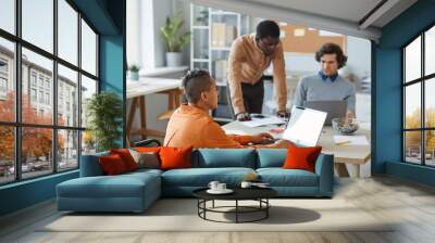 Portrait of black young woman with disability working in IT development company and using laptop during team meeting Wall mural