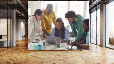 Portrait of contemporary multi-ethnic team leaning over laptop and smiling while working together in office, copy space Wall mural