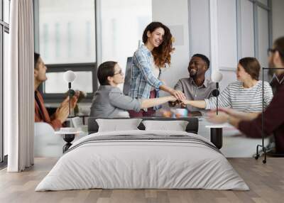 Portrait of creative business team stacking hands over meeting table, focus on smiling young woman standing in center Wall mural