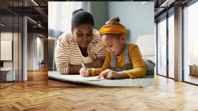 Portrait of cute African-American girl drawing on floor with mother in cozy home interior Wall mural