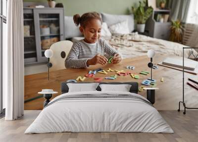 Portrait of cute African-American girl playing with letters while studying at home, copy space Wall mural