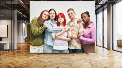 Portrait of group of friends from diverse backgrounds smiling and hugging each other in casual attire against plain white background emanating warmth and camaraderie Wall mural