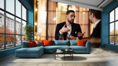 Portrait of handsome businessman discussing work with partner sitting at table in luxury restaurant, copy space Wall mural