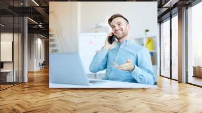 Portrait of handsome young man speaking by phone anile working in office and smiling happily, copy space Wall mural