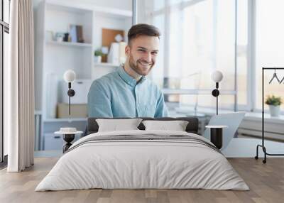 Portrait of handsome young man working in office and smiling happily at camera, copy space Wall mural