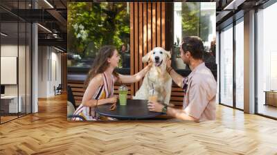 Portrait of happy couple with dog sitting at table together in outdoor cafe and laughing, copy space Wall mural